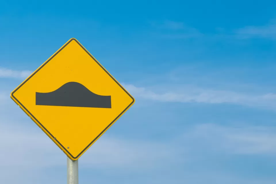 A yellow sign street sign showing the symbol for a speed bump: a simple black bump.